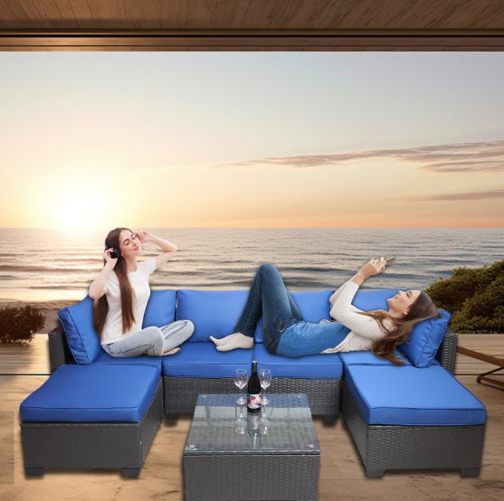 Outdoor sofa patio furniture set with blue cushions and wicker frame on wooden deck overlooking ocean