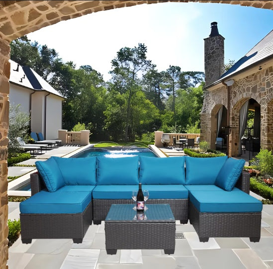 Blue cushioned outdoor sofa patio furniture set with wicker frame and glass-top coffee table on stone patio