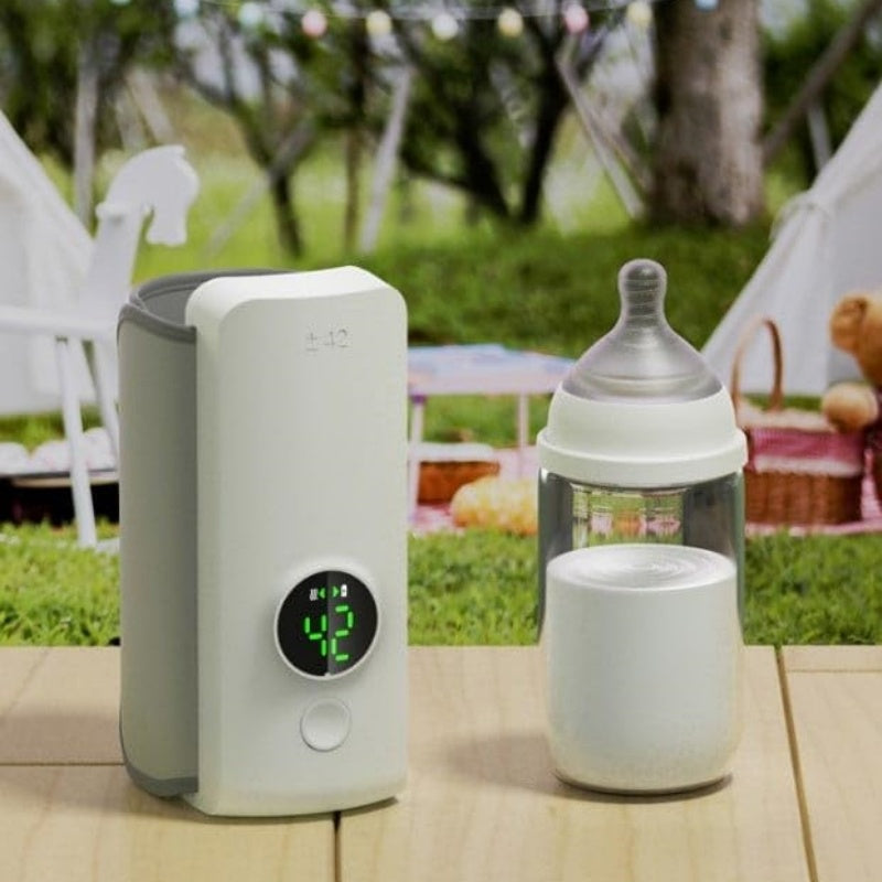 Shopi Vella portable baby bottle warmer in white with digital display next to a baby bottle on a wooden surface outdoors