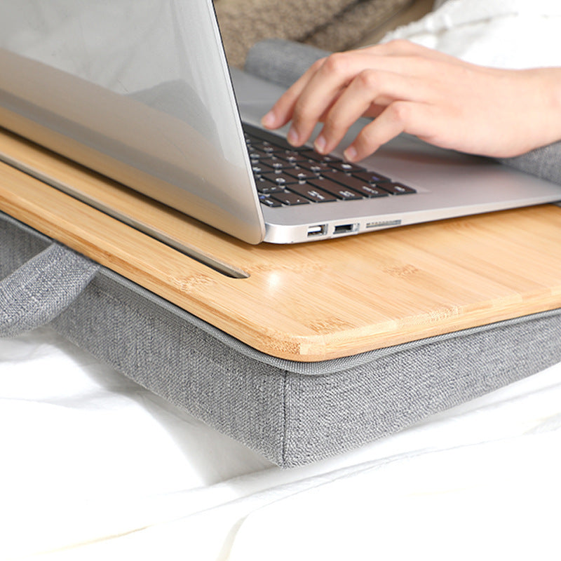 Portable computer desk for home with wooden surface and cushioned gray fabric base for comfortable laptop use
