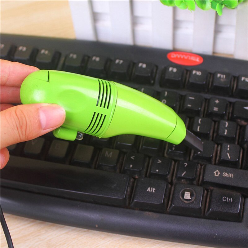 Green portable computer keyboard brush held over black keyboard for cleaning dust and debris