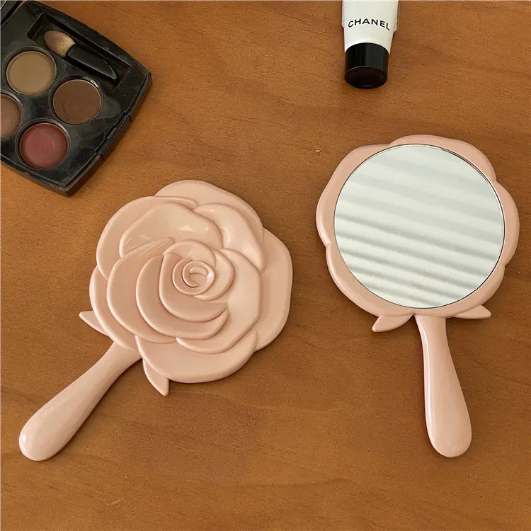 Pink rose-shaped portable cosmetic mirror for students with handle on wooden surface