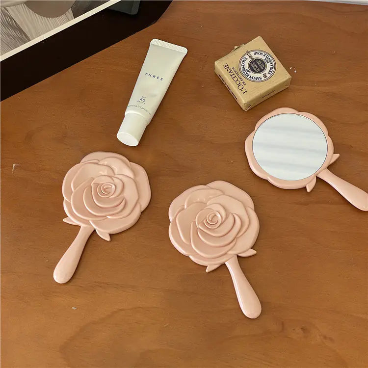 Pink rose-shaped portable cosmetic mirror for students placed on wooden table with skincare products