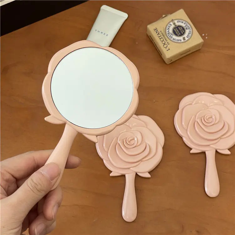 Portable cosmetic mirror for students with pink rose design handheld on wooden surface