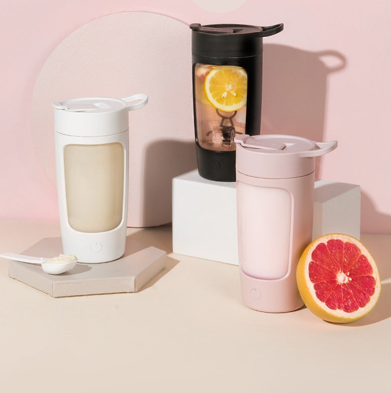 Shopi Vella portable juice blender in white black and pink with grapefruit and spoon on beige surface