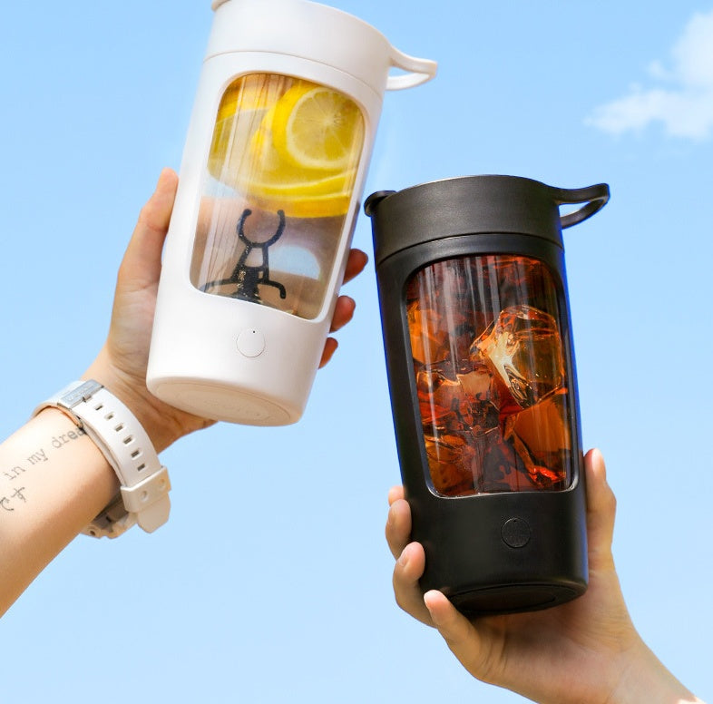 Shopi Vella portable juice blender in white and black with lemon slices and iced tea drinks held against blue sky