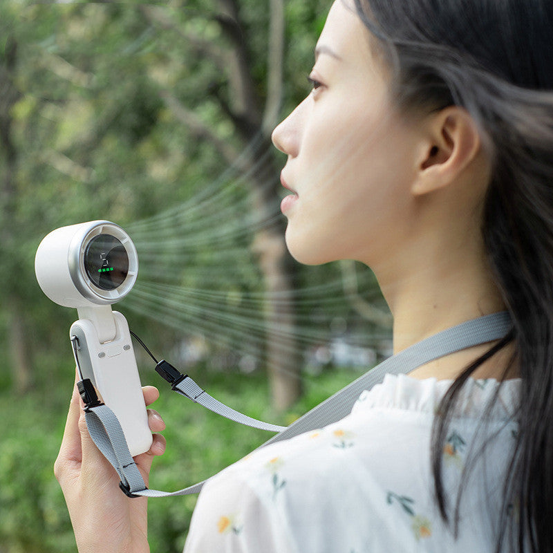 Shopi Vella portable mini fan rechargeable handheld with strap used outdoors by woman in white blouse
