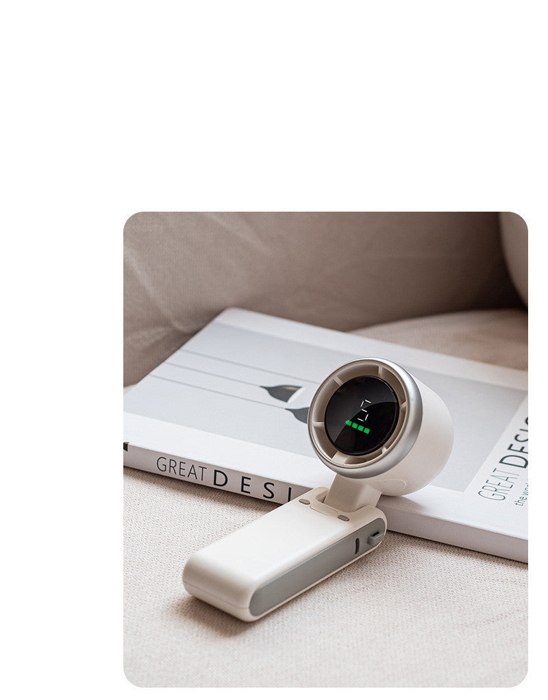 Shopi Vella portable mini fan rechargeable in white on a beige surface next to a design book