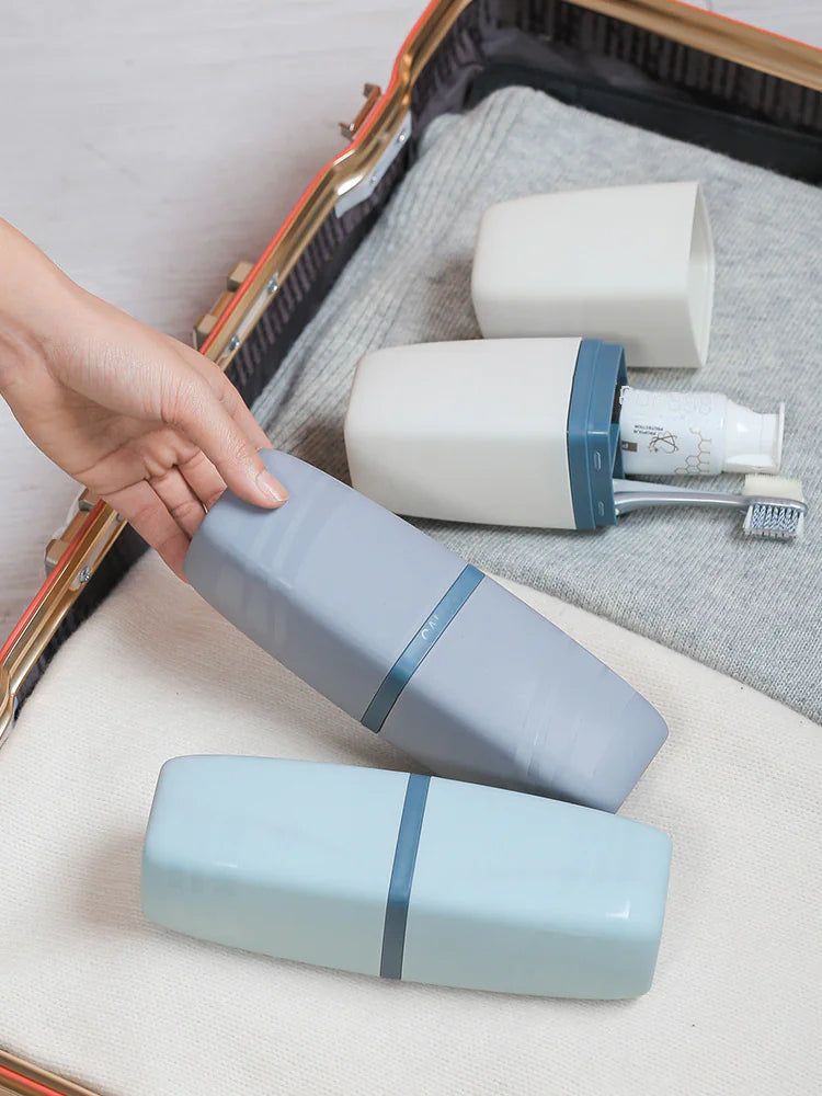 Portable toothbrush travel case in blue and gray colors shown packed in a suitcase with toiletries