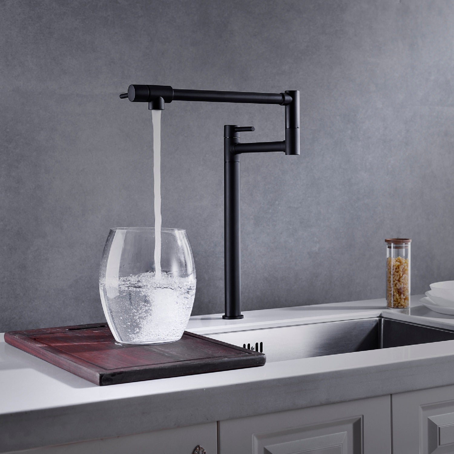 Shopi Vella pot filler faucet with extended handle in matte black filling water into a clear glass on kitchen countertop