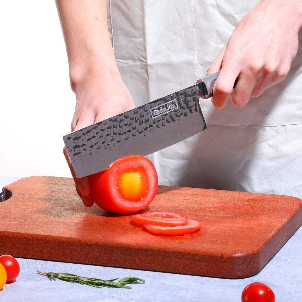 Hand forged vegetable knife with olivewood handle slicing a tomato on a wooden cutting board