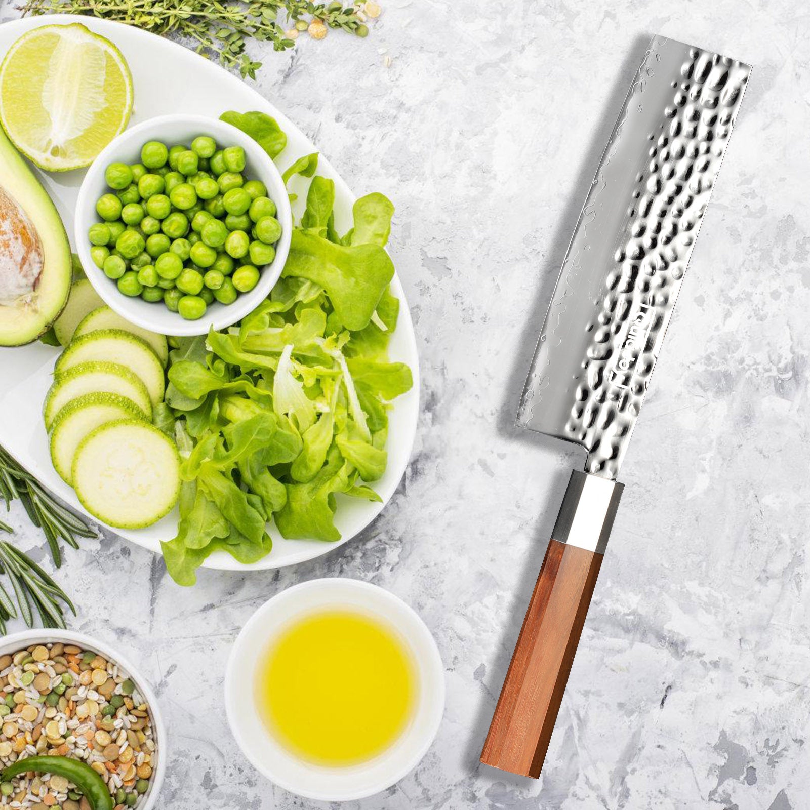 Hand forged vegetable knife with olivewood handle next to fresh vegetables and olive oil on a countertop