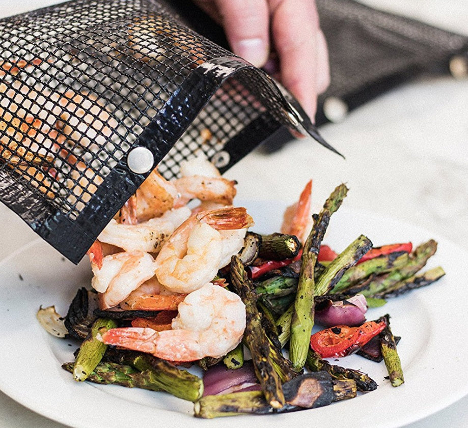 Reusable BBQ grill mesh bag from Shopi Vella with grilled shrimp and vegetables being poured onto a white plate