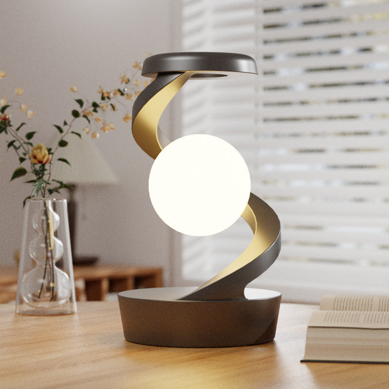 Rotating moon desk lamp with wireless charging on wooden desk near books and vase