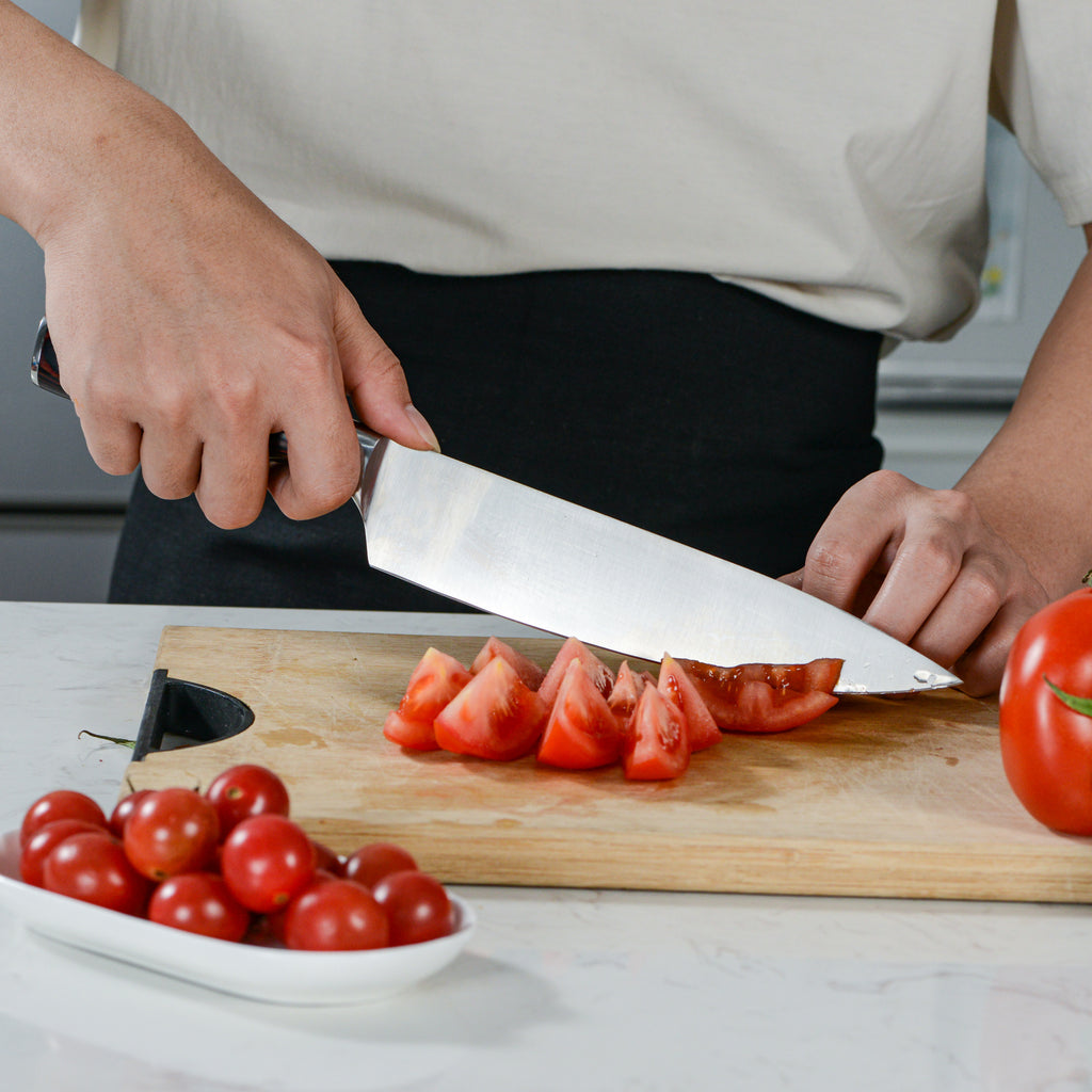 Person using sharp chef knife with sheath to cut tomatoes on wooden cutting board in kitchen