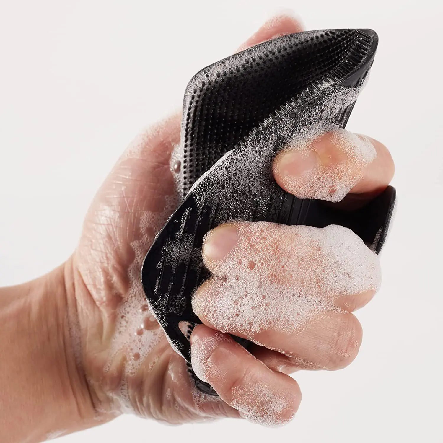 Hand holding black silicone bath brush with hook covered in soap foam for cleansing