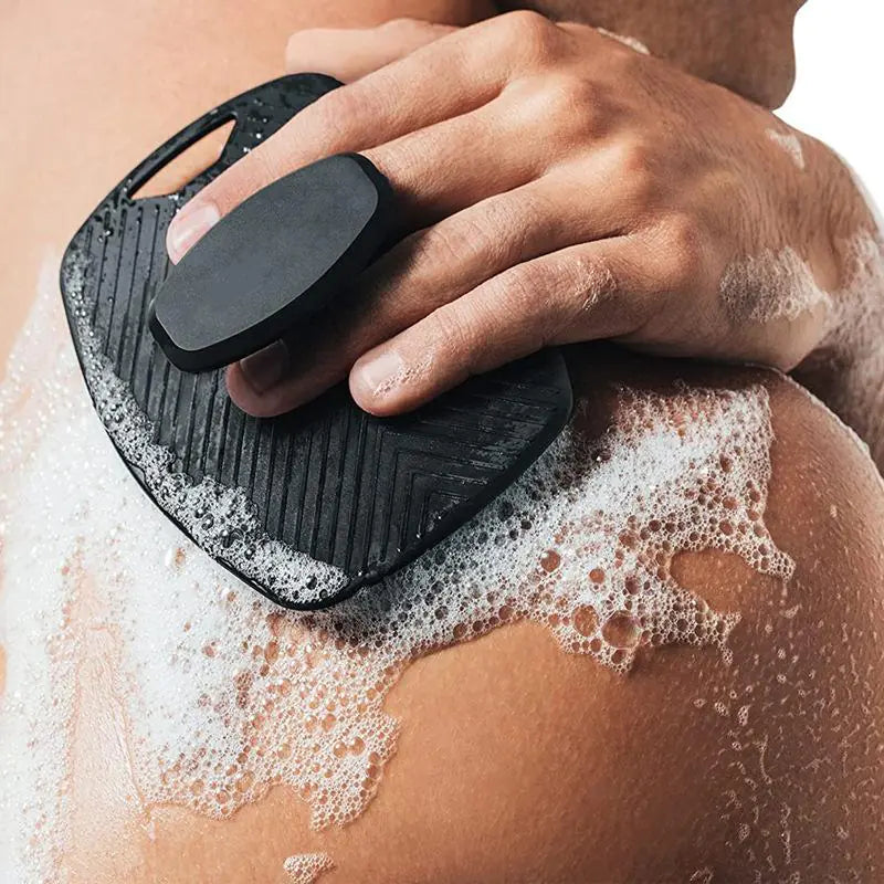 Black silicone bath brush with hook used for exfoliating skin with foam on shoulder