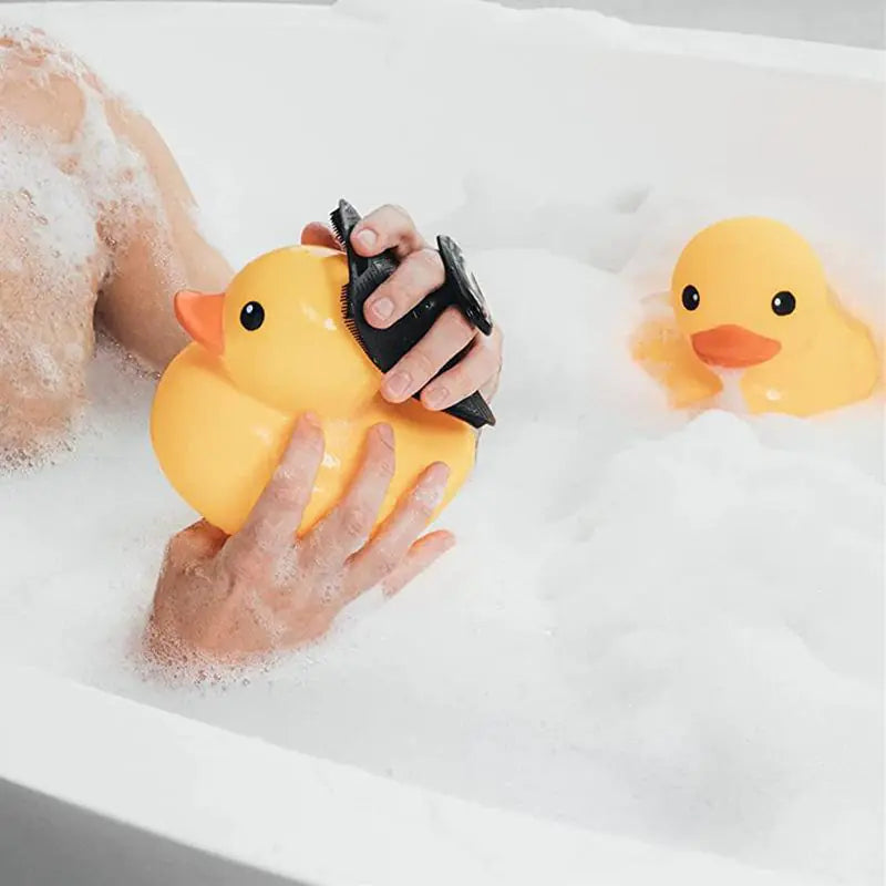 Yellow rubber duck with black silicone bath brush with hook held in a foam-filled bathtub