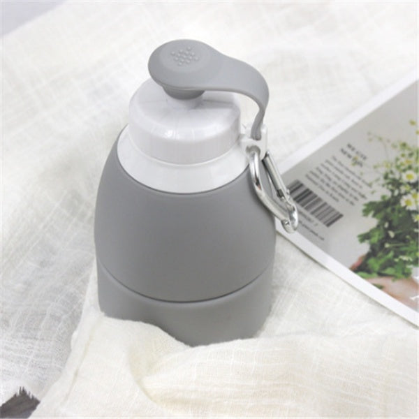 Gray silicone folding water bottle with white cap and carabiner clip on fabric surface