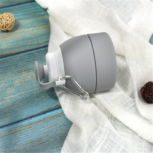Gray silicone folding water bottle by Shopi Vella with carabiner clip on white fabric background