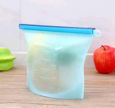 Shopi Vella blue reusable silicone food storage bag with measurement markings holding fruit on a wooden counter