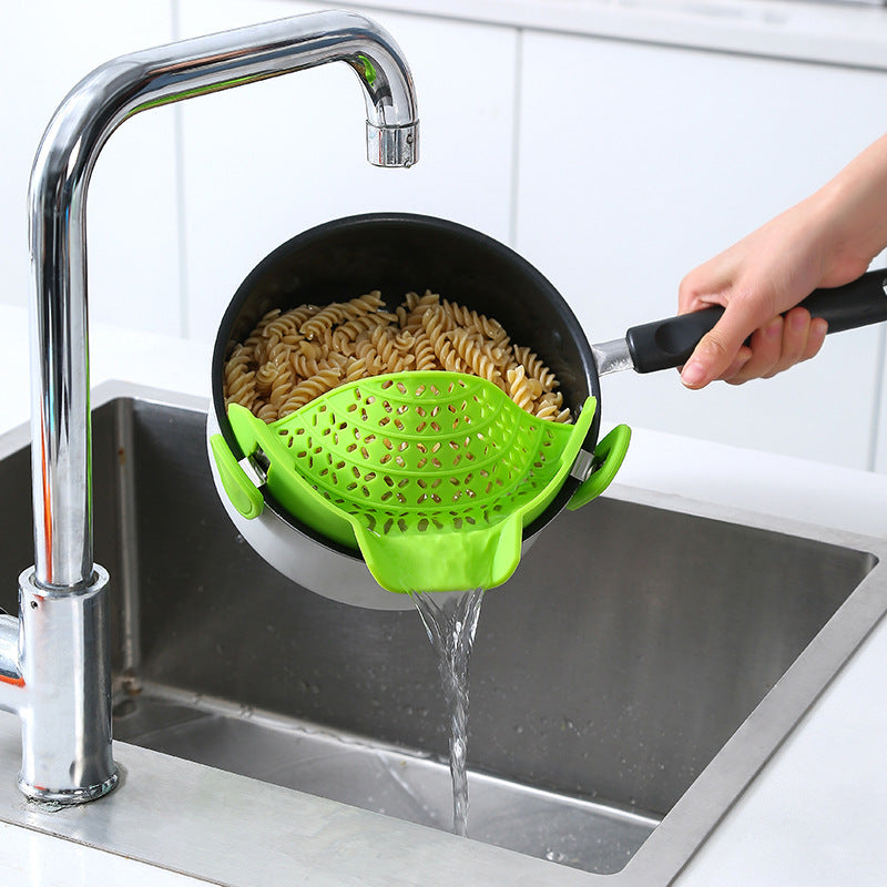 Green silicone pot side drain stopper draining water from pot with pasta over kitchen sink