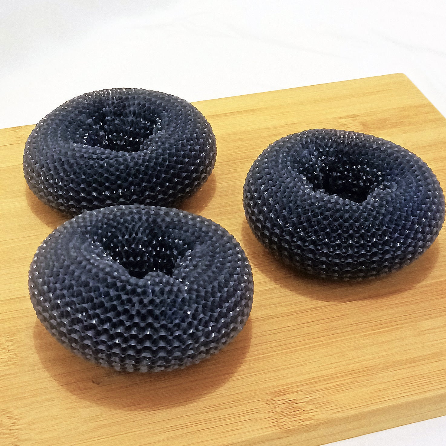 Set of three black circular scrubbing pads for kitchen storage on a wooden surface