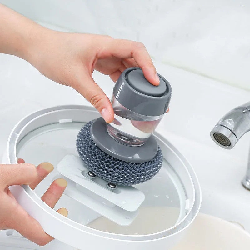 Shopi Vella soap dispensing kitchen brush with grey scrubber being held above a sink for cleaning