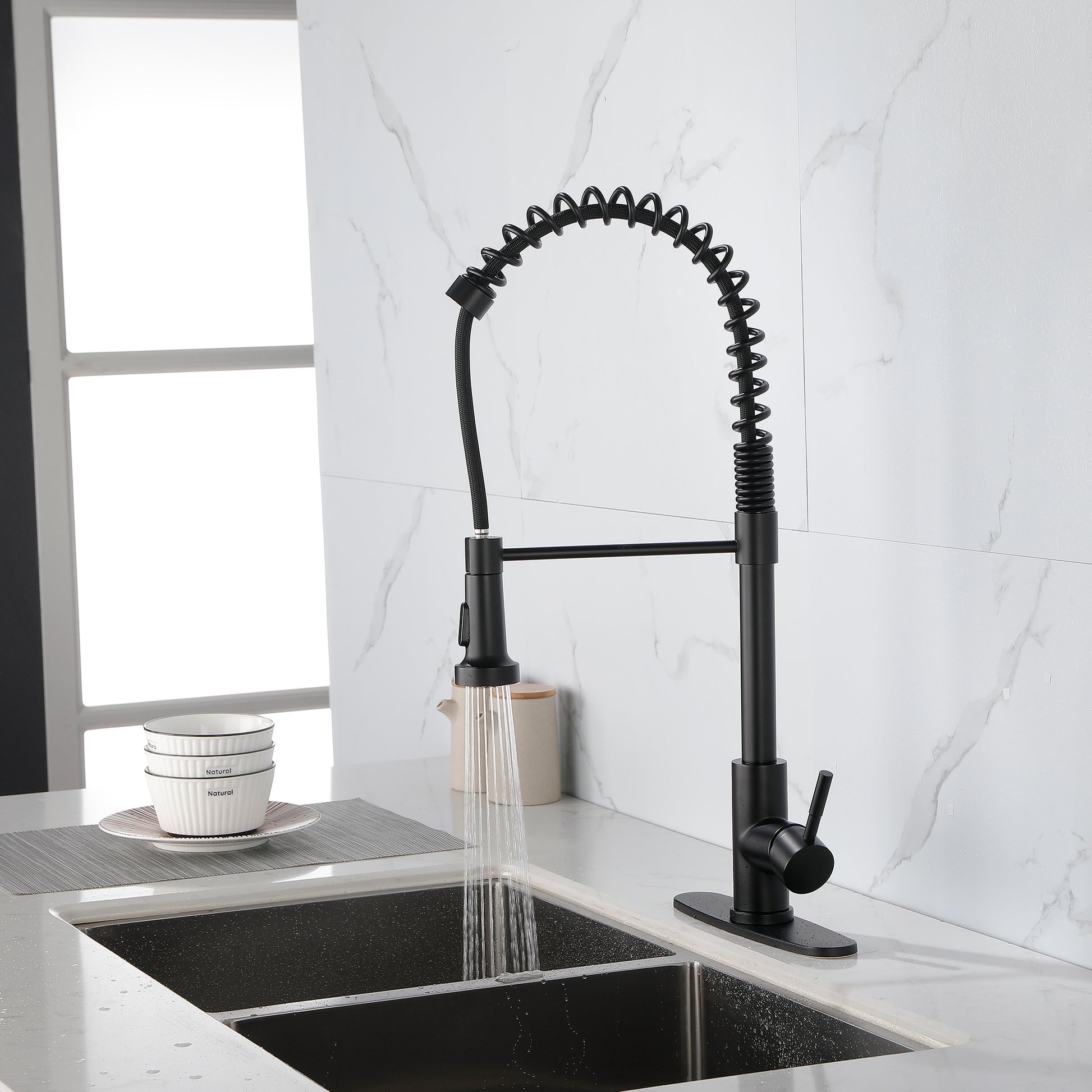 Matte black solid brass kitchen faucet with flexible spring neck installed on white marble countertop