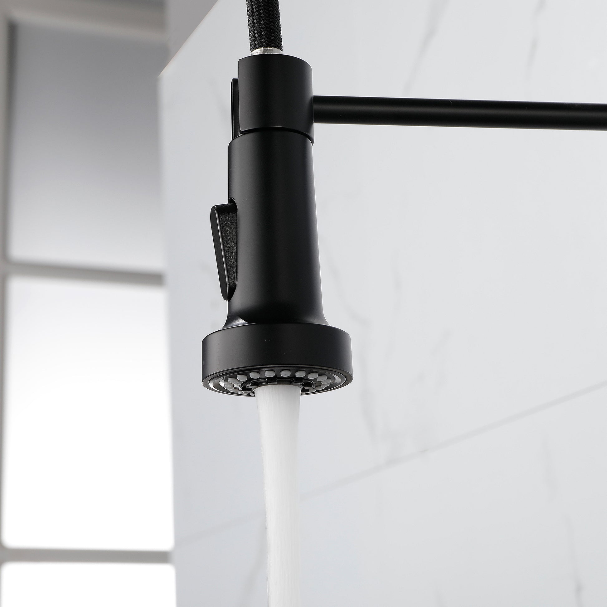 Black solid brass kitchen faucet with pull-down sprayer and water running in modern kitchen