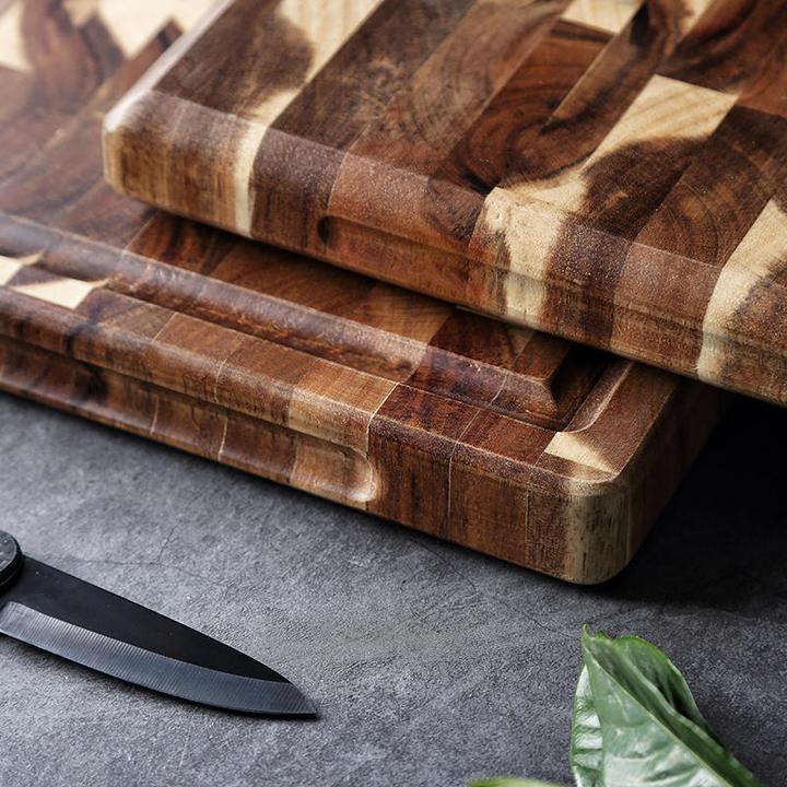 Shopi Vella solid wood cutting board with natural grain pattern beside kitchen knife and greens