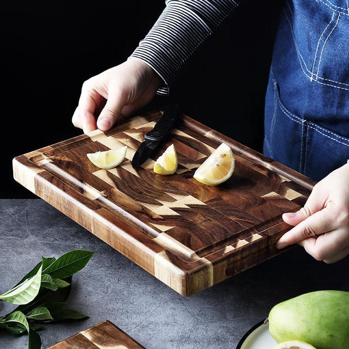 Shopi Vella solid wood cutting board with juice groove and geometric pattern held by person with lemon wedges