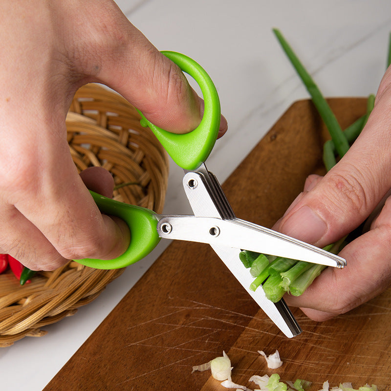 Green-handled stainless steel herb scissors cutting fresh herbs over wooden chopping board