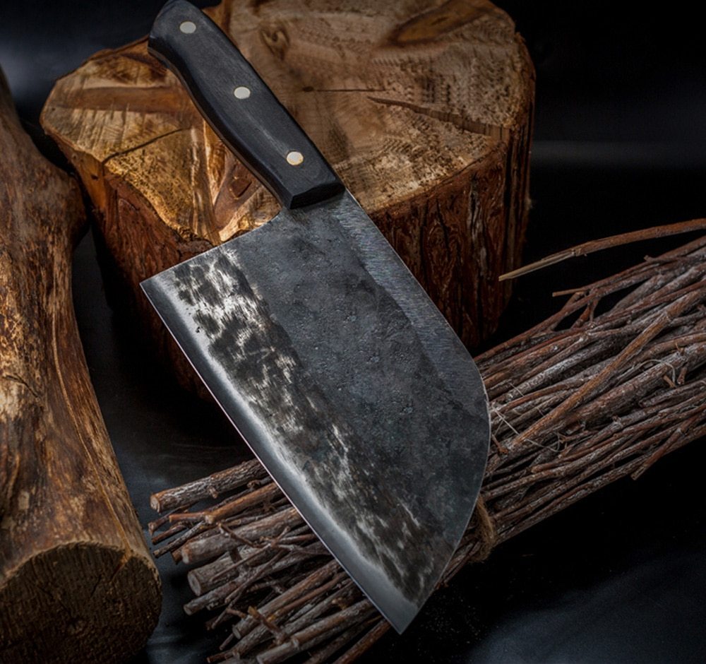 Shopi Vella stainless steel meat cleaver with wooden handle resting on wooden logs and branches