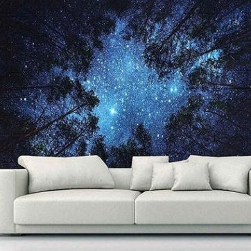 Starry forest tapestry wall hanging with night sky and trees above white couch in modern living room