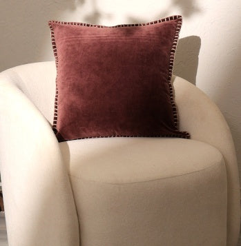 Shopi Vella stonewashed cotton velvet throw pillow in dark rose on a white cushioned chair