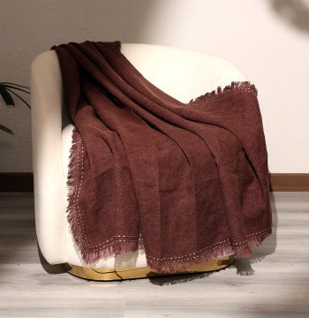Shopi Vella stonewashed linen throw blanket in rich brown draped over a modern white armchair