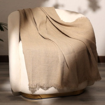 Stonewashed linen throw blanket draped over a white modern chair showcasing natural texture and soft fringed edges
