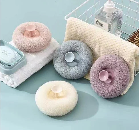 Set of four suction bath exfoliating brush set in pastel colors with a soap bar and towel on a blue surface