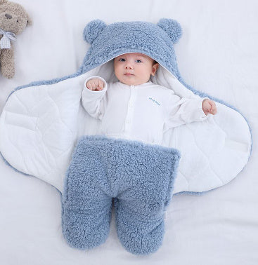 Baby wrapped in a blue thick winter baby quilt with hood and bear ears lying on white blanket