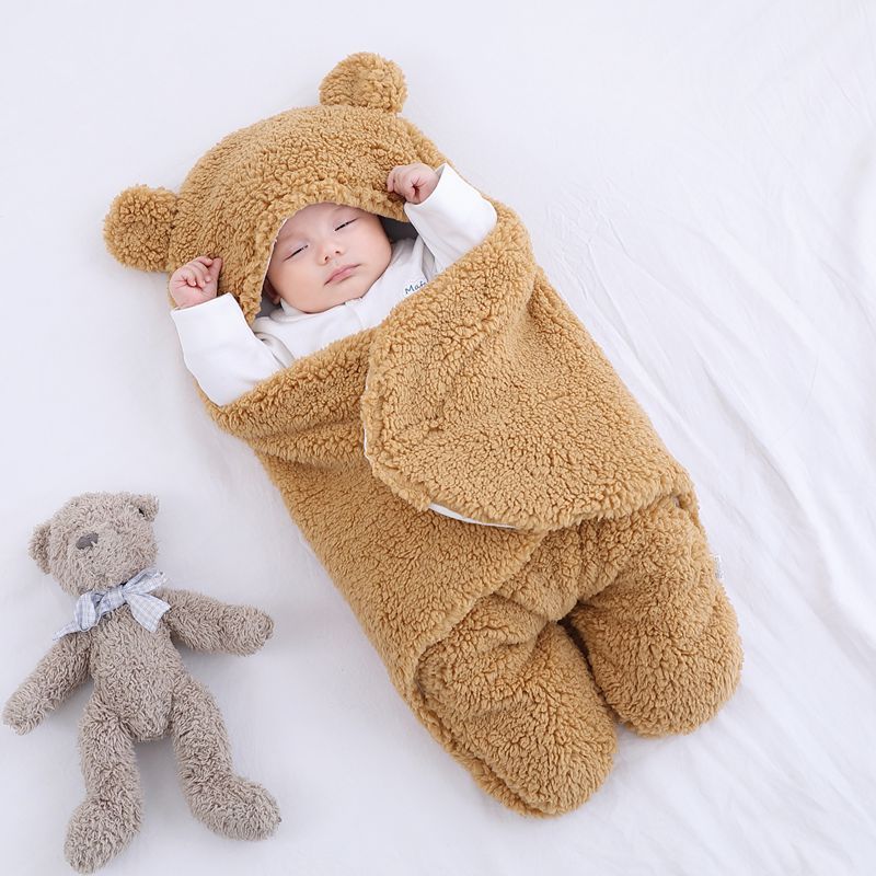 Baby wrapped in a thick winter baby quilt with bear ears hood lying next to a stuffed teddy bear
