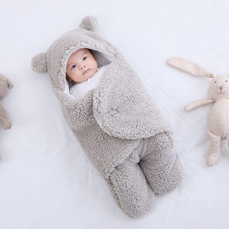 Baby wrapped in a thick winter baby quilt with hood and bear ears lying on white bedding