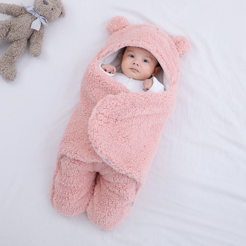 Baby wrapped in a pink thick winter baby quilt with bear ears hood lying on white bedding