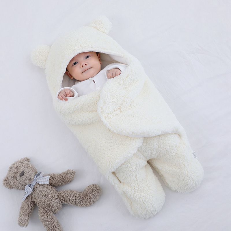 Baby wrapped in a soft cream thick winter baby quilt with bear ears hood lying next to a plush teddy bear