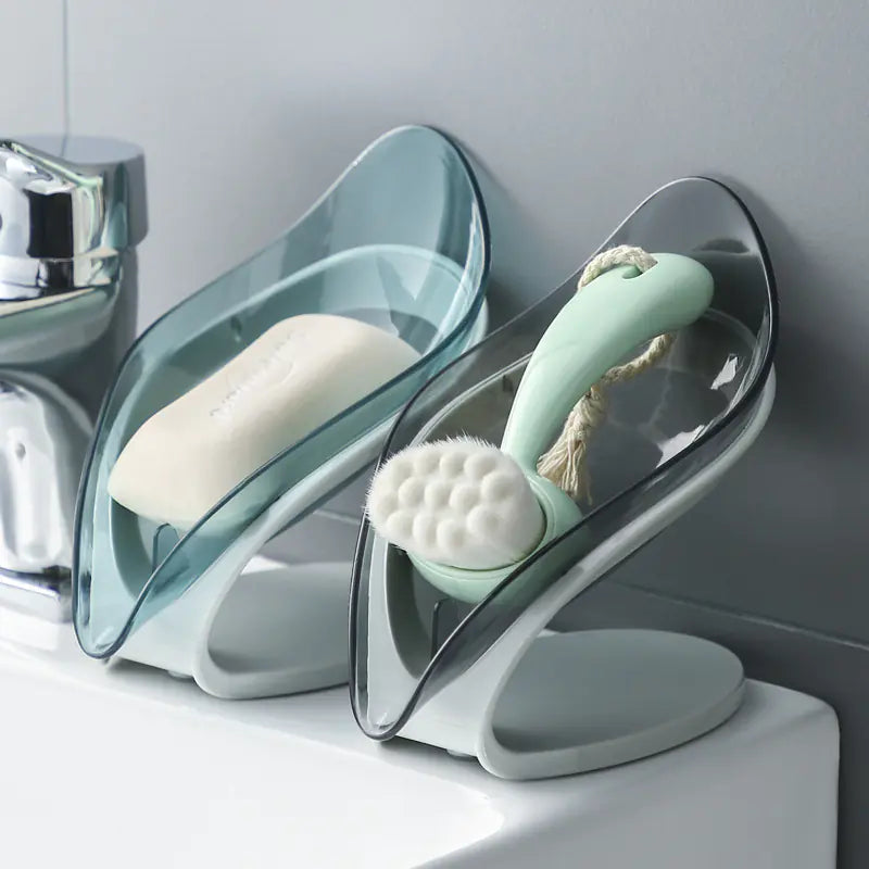 Transparent leaf soap holder mounted on bathroom wall holding soap and a brush