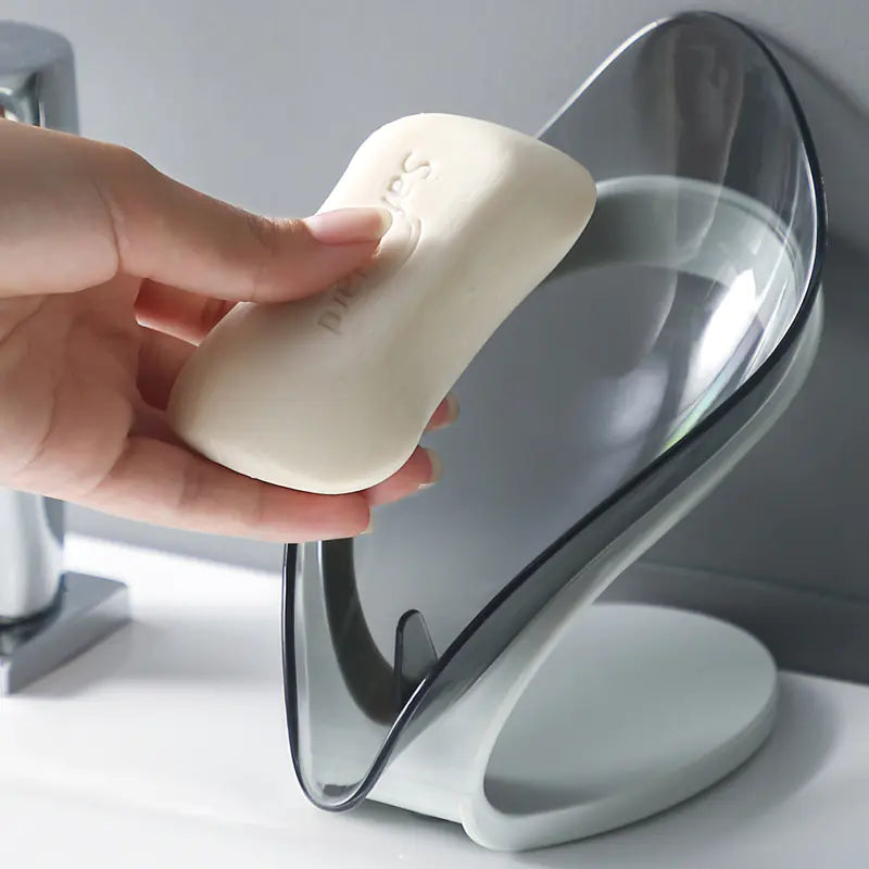 Hand placing white soap on a transparent leaf soap holder with curved design on bathroom counter