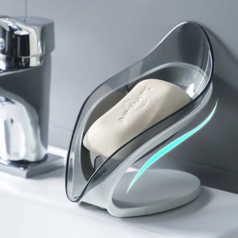 Transparent leaf soap holder with a white soap bar placed on a bathroom sink next to a chrome faucet