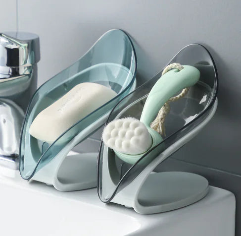 Transparent leaf soap holder with curved design on bathroom sink holding soap and scrub brush