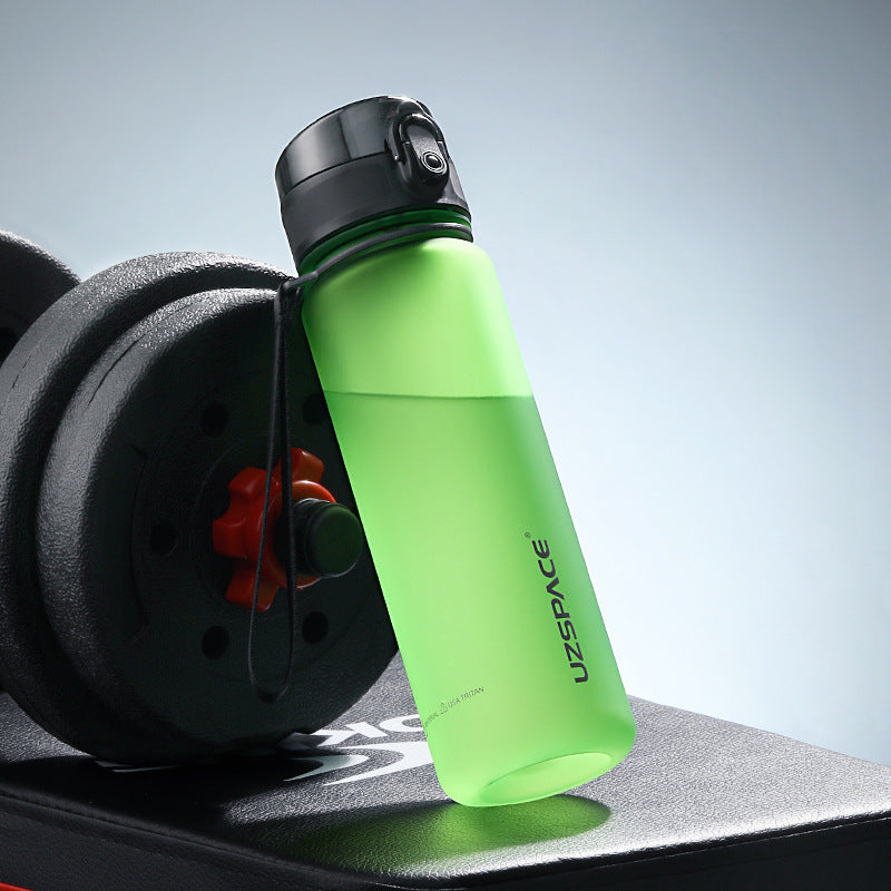 Shopi Vella colorful sports water bottle in green with black cap next to dumbbell on workout bench