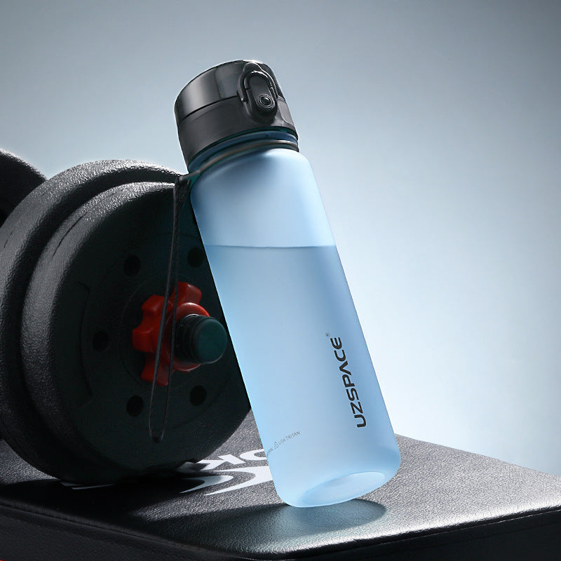 Shopi Vella colorful sports water bottle translucent blue with black flip cap beside gym weights